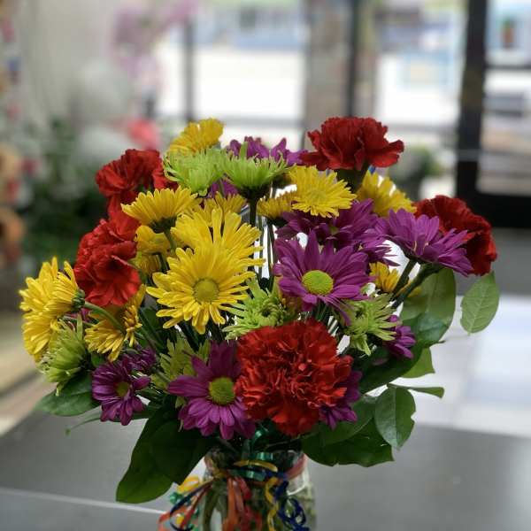 Colorful bouquet of daisies and carnations in a glass vase with ribbon curls
