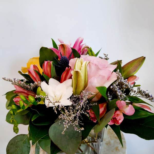 Mixed bouquet with pink lilies, roses, and white blooms in a glass vase
