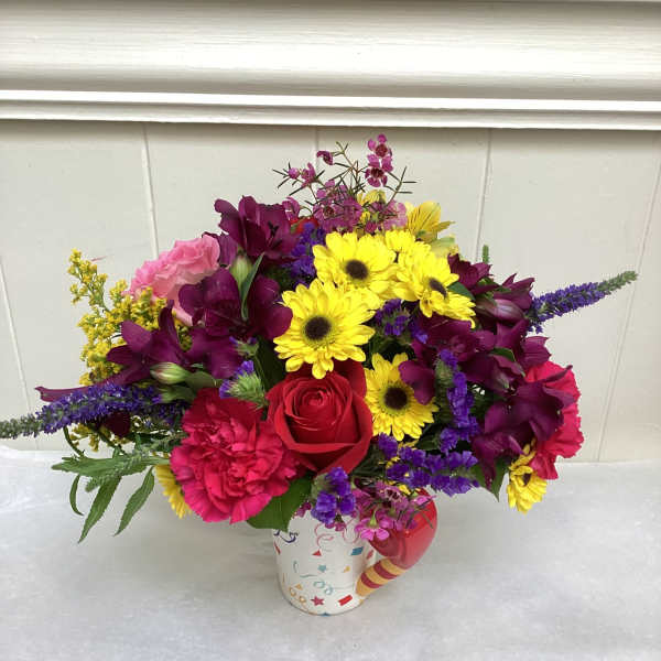 Bright mixed flower arrangement in a colorful patterned mug-style container