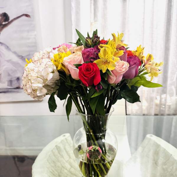 Mixed bouquet of roses, hydrangea, and yellow lilies in a glass vase