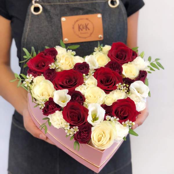 Heart-shaped box of red, white, and cream roses held by a person