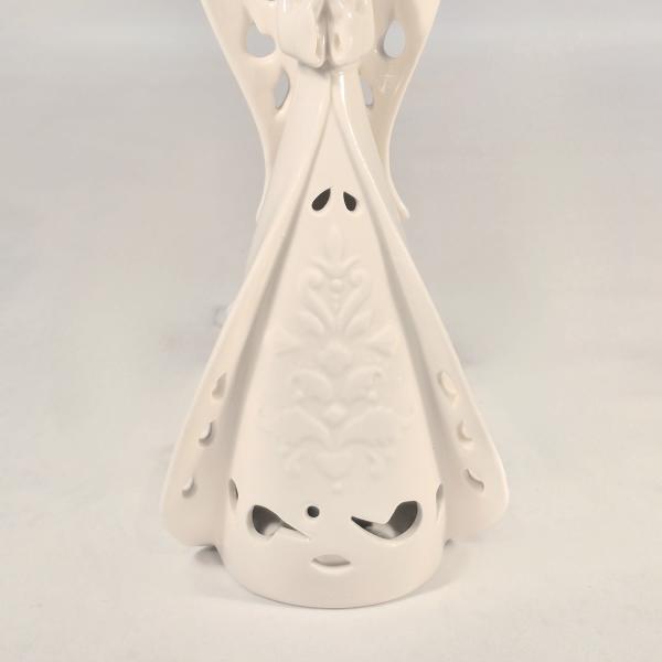 White ceramic angel figurine with cutout wings and patterned gown against a plain background