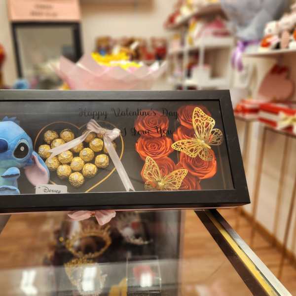 Framed gift box with a Stitch plush, chocolates, and orange roses