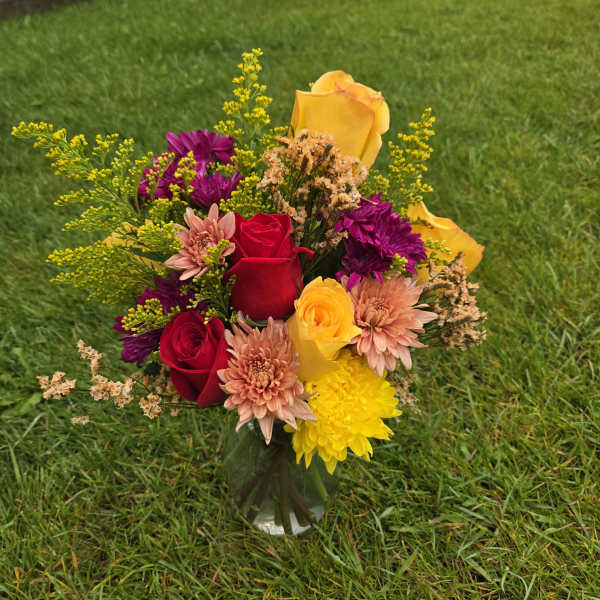 Mixed bouquet of red and yellow roses with purple and peach flowers in a glass vase