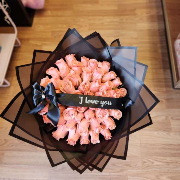 Bouquet of peach-pink roses wrapped in black paper with a ribbon