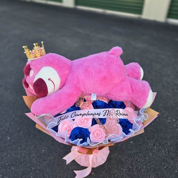 Pink teddy bear resting on a bouquet of pink and blue roses
