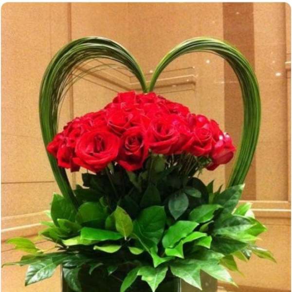 Red roses arranged in a heart-shaped basket with green foliage