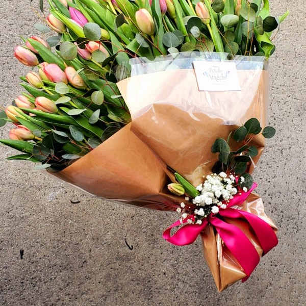 Large bouquet of pink and peach tulips wrapped in brown paper with a bright pink ribbon