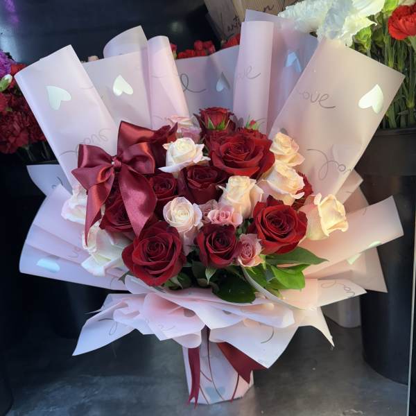 Bouquet of red and pink roses wrapped in pale pink paper with a burgundy bow