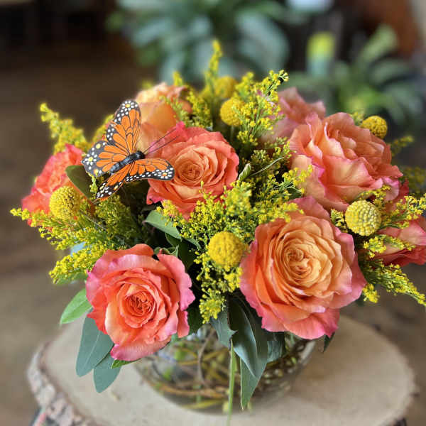 Bouquet of coral roses with yellow filler flowers in a glass vase