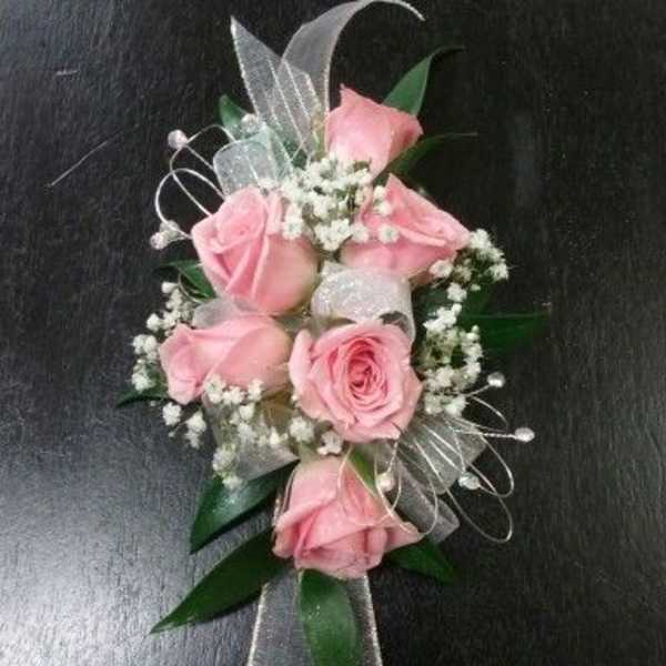 Pink rose corsage with baby's breath and silver ribbon on a dark background