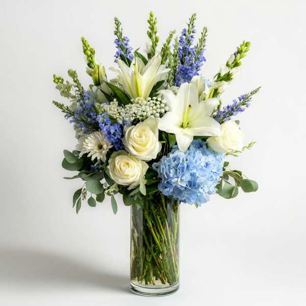 Bouquet of white lilies, cream roses, blue hydrangea, and purple flowers in a glass vase