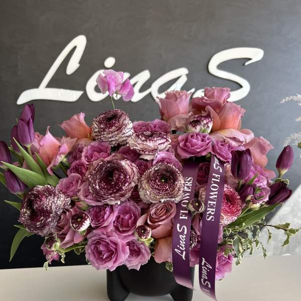 Pink and purple bouquet in a black vase with ribbon tags