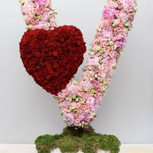 Tall pink floral V sculpture with a red rose heart on a moss-covered rectangular base