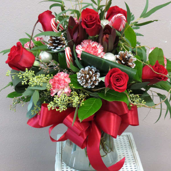 Red roses and candy canes arranged in a glass vase with a red ribbon