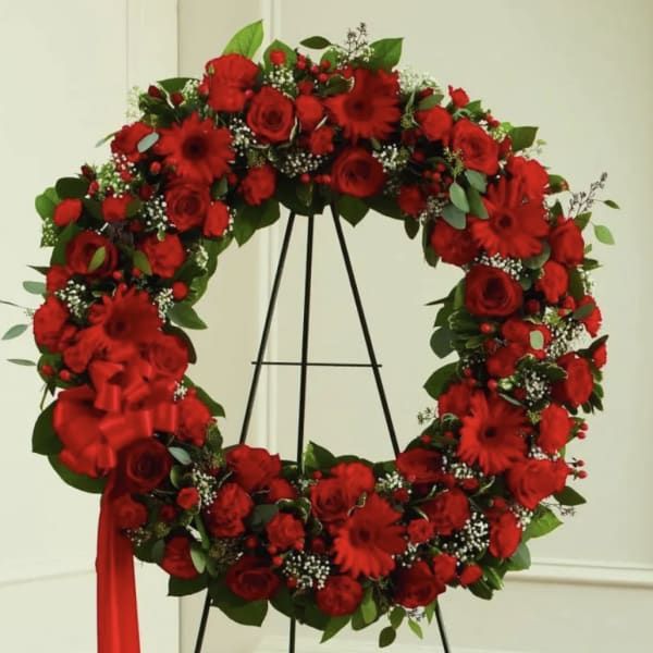 Large red floral wreath on a black stand with a ribbon