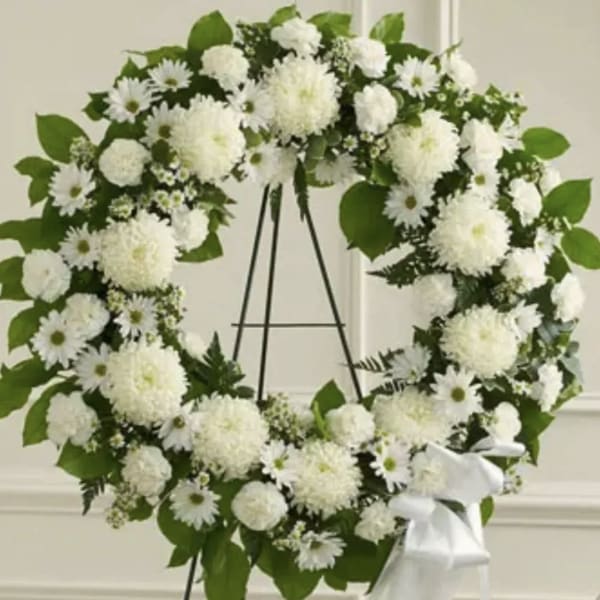 White floral wreath on a black easel with a white ribbon