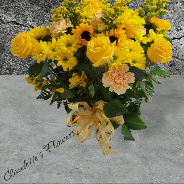 Yellow roses and daisies arranged with peach carnations and a ribbon bow