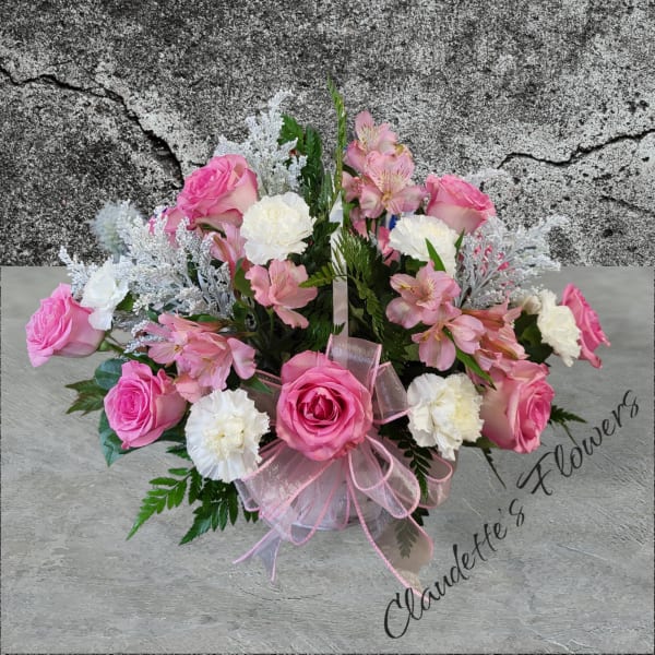 Pink roses and white carnations arranged in a basket with a pink ribbon