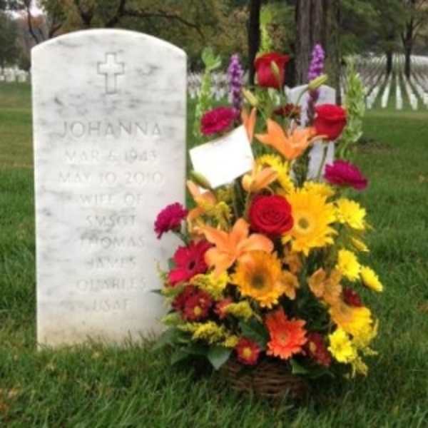 Colorful basket of yellow, orange, and red flowers placed beside a white cemetery headstone