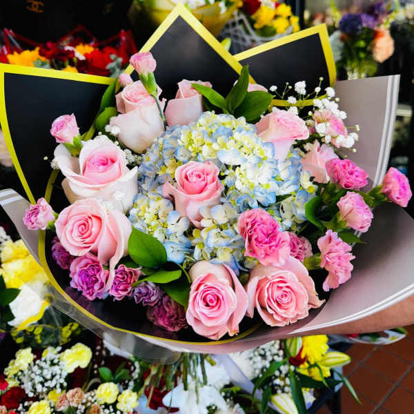 Hand-tied bouquet of pink roses and sprays with blue and white hydrangeas in decorative wrap