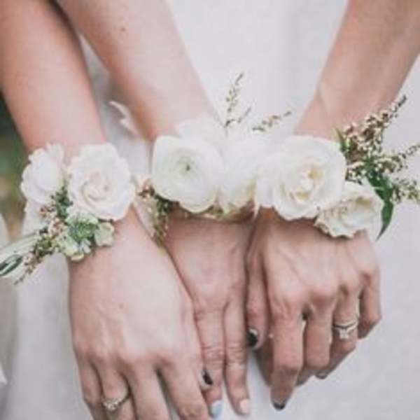 Hands wearing white floral wrist corsages with small white blooms