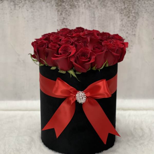 Round black hatbox of red roses wrapped with a red satin bow and jeweled brooch.