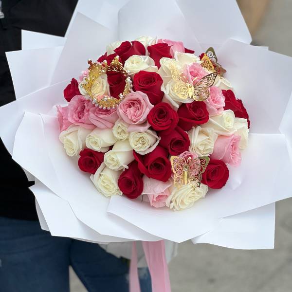 Large bouquet of red, white, and pink roses wrapped in white paper with gold butterflies and a crown