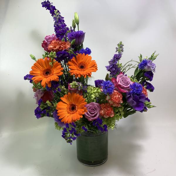 Colorful mixed bouquet in a glass vase with orange gerberas and purple blooms