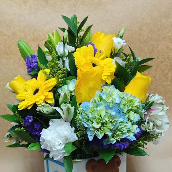 Bright mixed arrangement of yellow and blue flowers in a cube vase with a baby bear and letter C block design