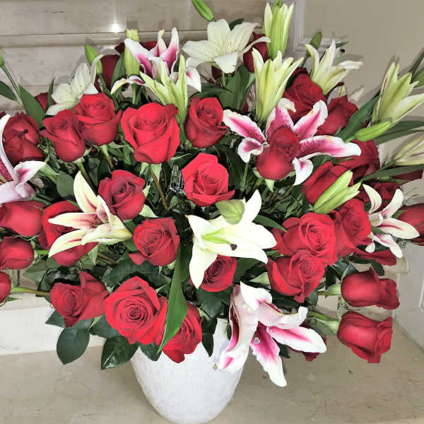 Large arrangement of red roses with white and pink lilies in a white ceramic vase