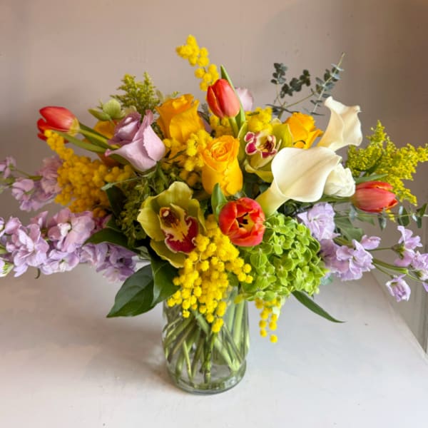 Bright mixed bouquet with yellow roses, red tulips, white calla lilies, orchids and stock in a clear glass vase