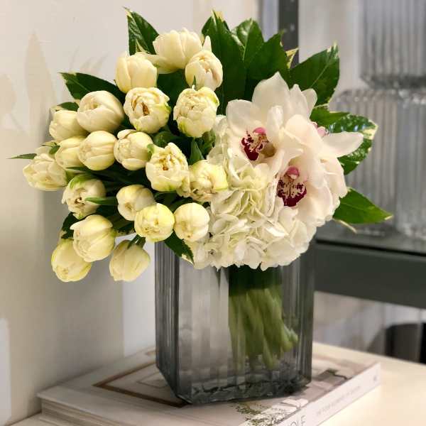 White tulips, hydrangeas, and an orchid arranged in a tall gray glass vase.