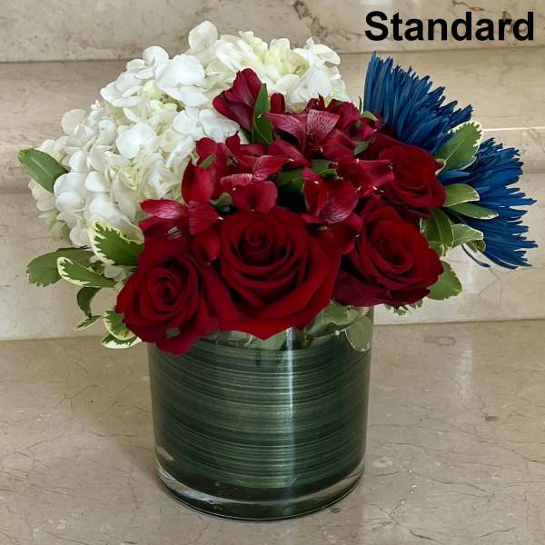 Red roses, white hydrangeas, and blue daisies in a glass vase