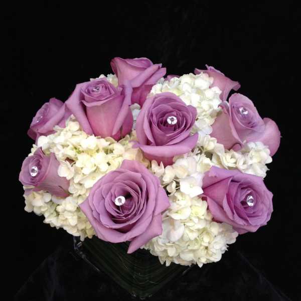 Lavender roses arranged with white hydrangeas in a clear vase