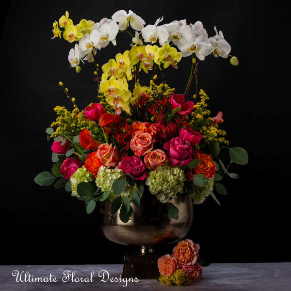 Tall floral arrangement with orchids, roses, and tulips in a metallic vase
