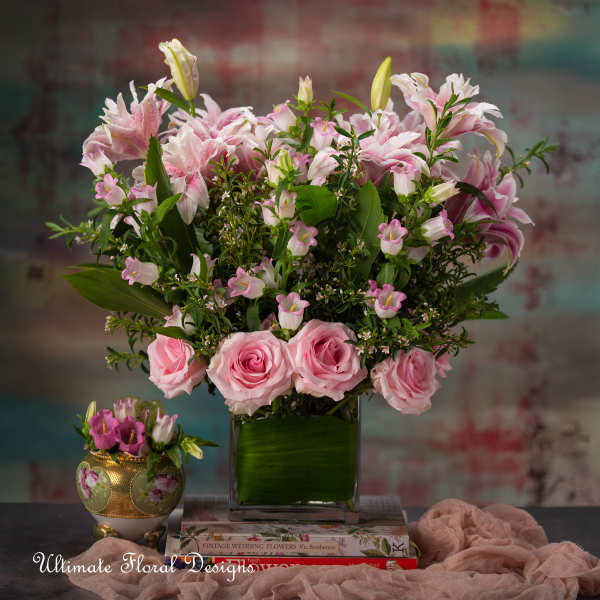 Pink roses and lilies arranged in a square glass vase