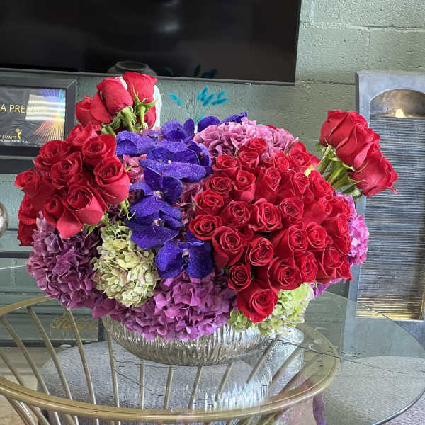 Large bouquet of red roses, purple orchids, and hydrangeas in a glass bowl vase