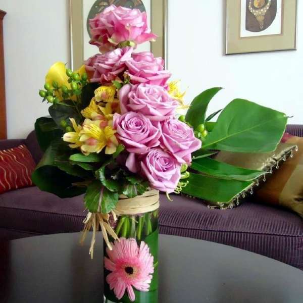Pink roses and yellow flowers arranged in a tall glass vase