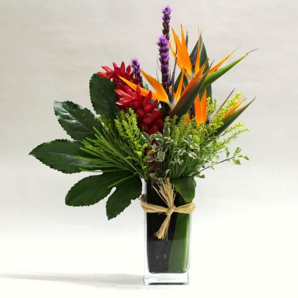 Tropical flower arrangement in a tall glass vase with orange and red blooms