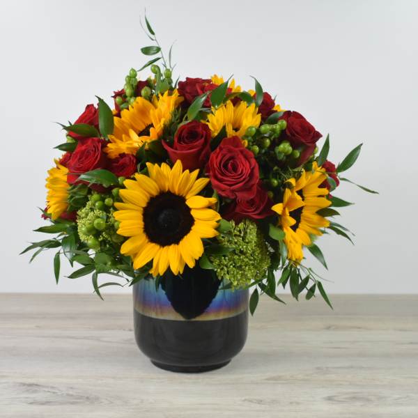 Bouquet of red roses and yellow sunflowers in a dark vase