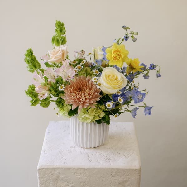 Pastel arrangement of daffodils, roses, chrysanthemum and mixed flowers in a white ribbed vase
