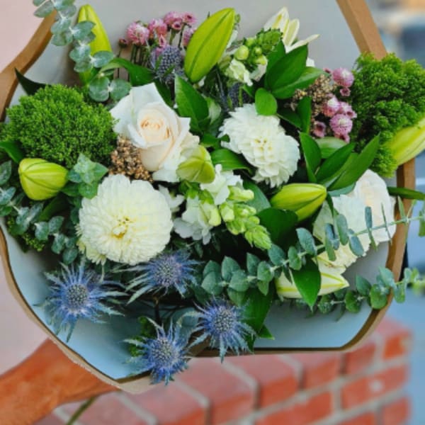 Bouquet of white and green flowers with blue thistle in wrapped paper