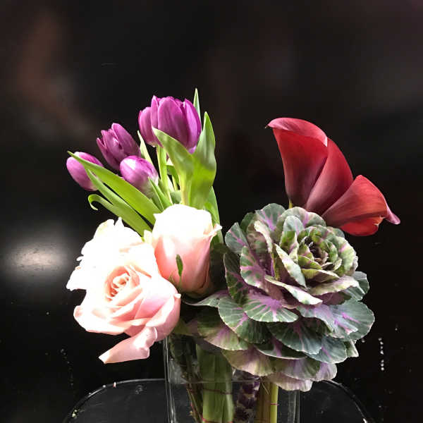 Mixed bouquet with pink roses, purple tulips, and a red calla lily in a glass vase