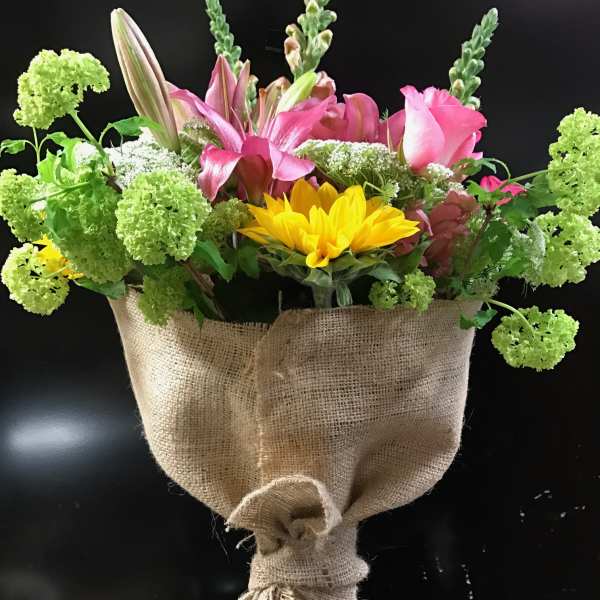 Bouquet of pink lilies and yellow sunflowers wrapped in burlap