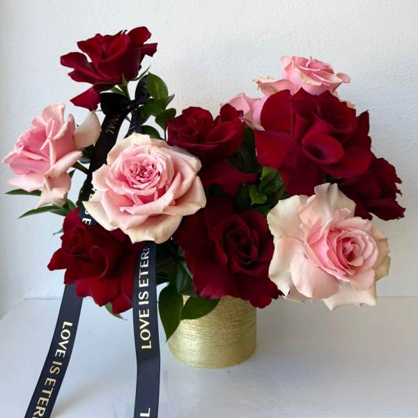 Pink and red roses arranged in a gold vase with black ribbons
