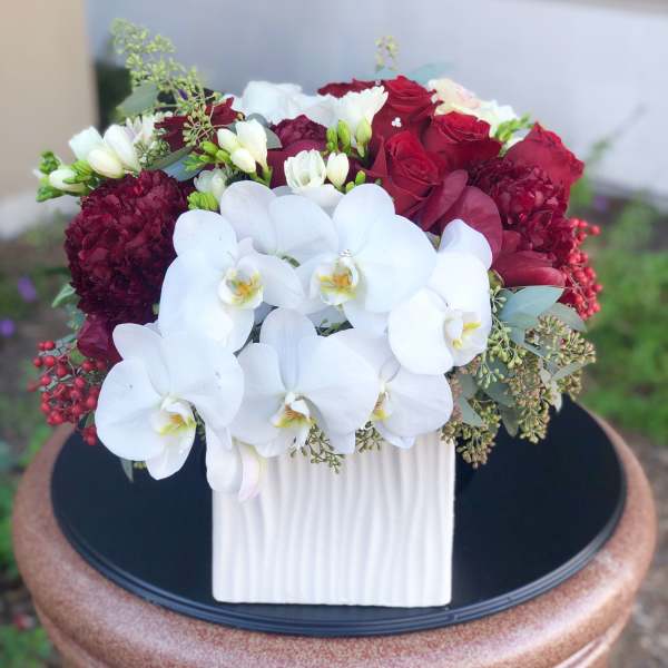 White orchids and red roses in a ribbed white vase