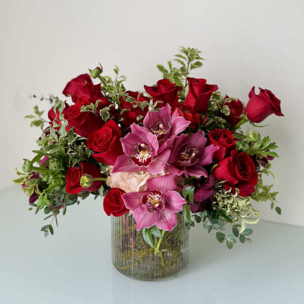 Red roses and pink orchids arranged in a glass vase