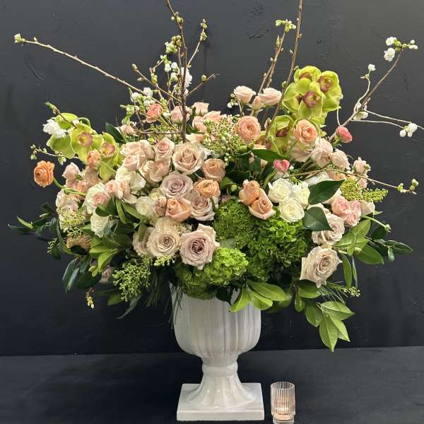 Large floral arrangement in a white pedestal vase with pink roses and green orchids