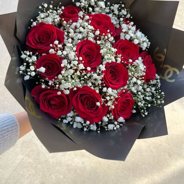 Handheld bouquet of red roses and white filler flowers wrapped in dark black paper
